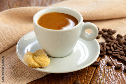 xícara de café em close com biscoito no pires em fundo de madeira.