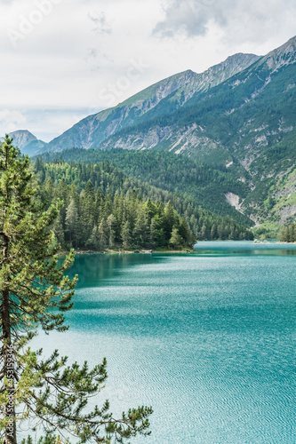an emerald green waters of Blindsee lake, pine tree in a foreground and mountains in a background