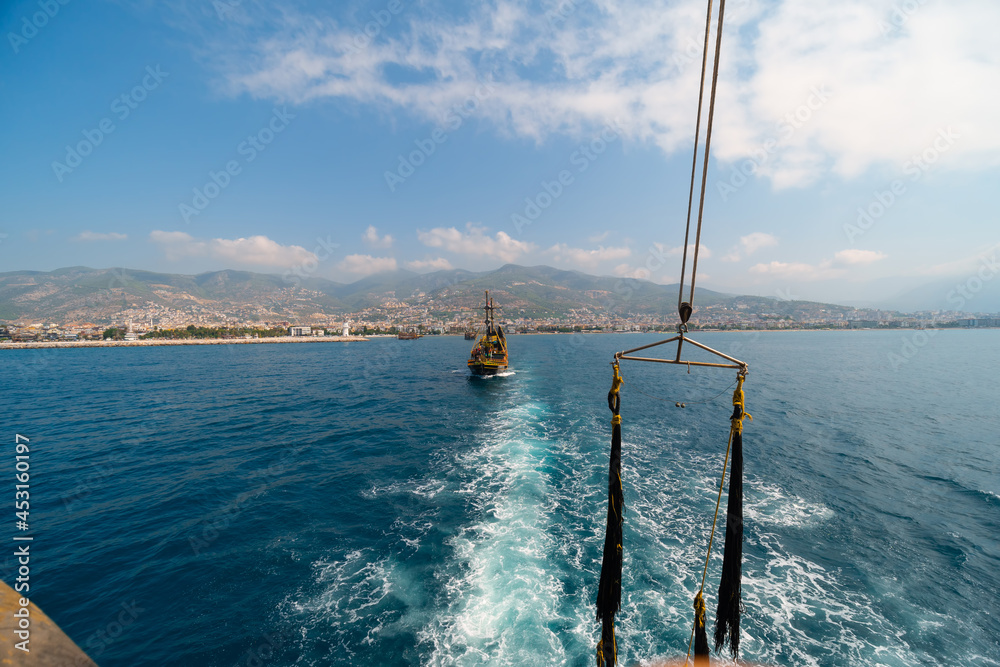 Old pirate ship on the water of Mediteranean sea. Tourist entertainment, coastal tour. Summer sunny day. Mountain shore of Alanya. Turkey.