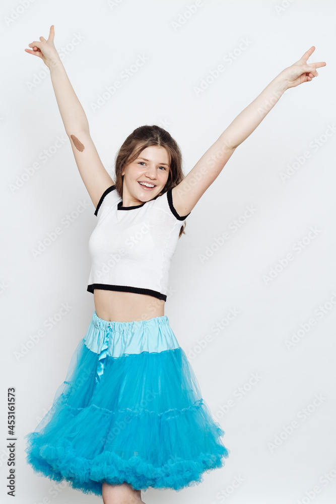 Cheerful teenager girl with curly hair wearing blue fluffy skirt and white t shirt posing on white background. Emotions Cheerful teenager girl with curly hair wearing blue fluffy skirt and white t shirt posing on white background. Emotions
