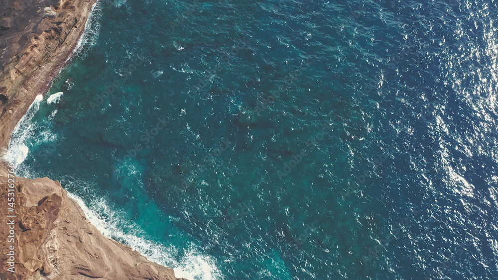 Aerial shot from drone. Top view on the rocky ocean shore.. Blue Waves of the Pacific Ocean is crashing on the rock. White sea foam. Volcanic beach of Tropical Island Oahu Hawaii. Aerial shot from drone. Top view on the rocky ocean shore.. Blue Waves of the Pacific Ocean is crashing on the rock. White sea foam. Volcanic beach of Tropical Island Oahu Hawaii.