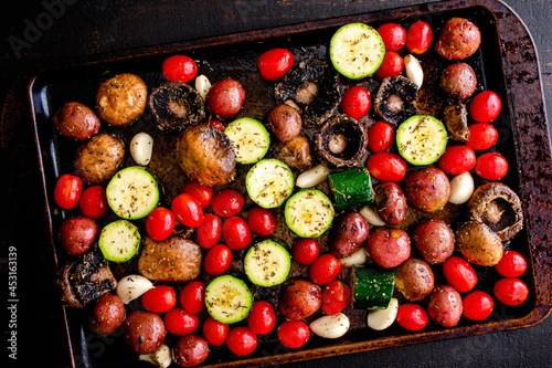 Uncooked Italian Vegetables Tossed in Olive Oil and Spices: Raw grape tomatoes, zucchini, mushrooms, red potatoes, garlic cloves on a sheet pan photo