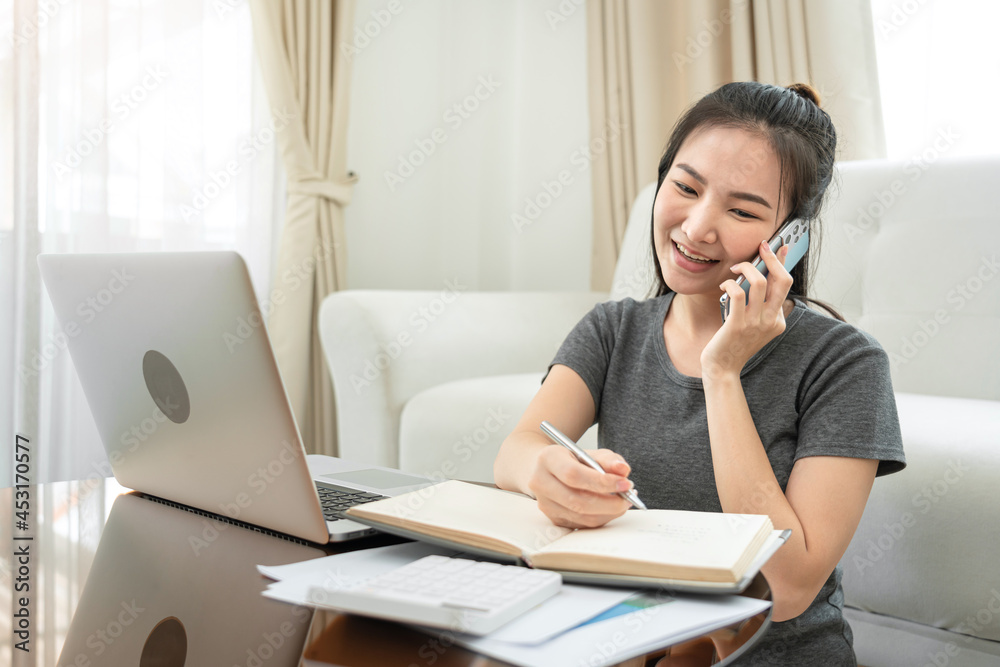 Asian freelance woman using smartphone to receive order from client and writing information on notebook Asian freelance woman using smartphone to receive order from client and writing information on notebook