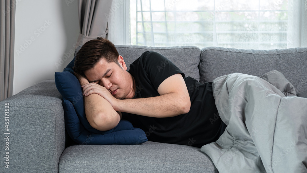 Asian man is lying with blanket on couch at home to rest when feeling sick from high fever, migraine Asian man is lying with blanket on couch at home to rest when feeling sick from high fever, migraine