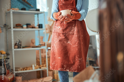 Female potter in apron holding handmade clay bowl