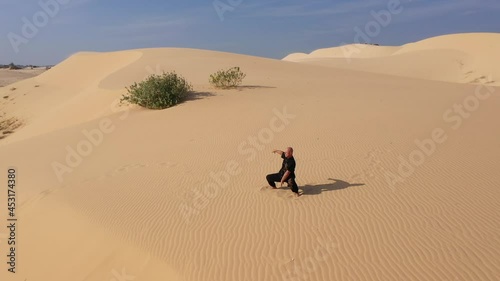 Old man in black is engaged in kung fu in the dunes at sunset. a lot of sand, golden sunset light. sports training. handsome man meditating. sensei training in desert. aerial view