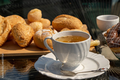 Outdoor afternoon tea  served in a white cup  silver spoon with white detail  bread  jam and chocolate donut in the background