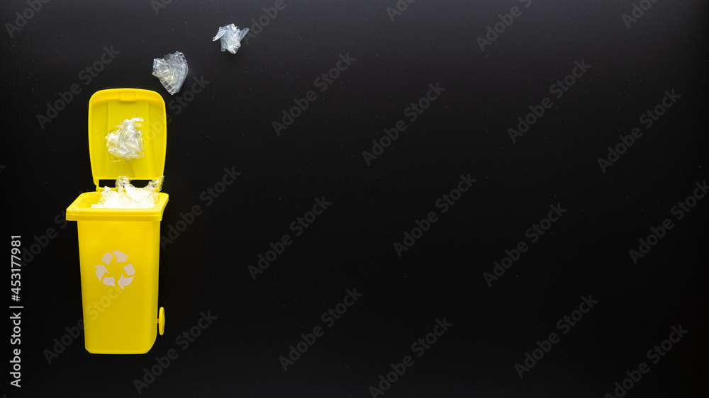 Recycling plastic sorting. Bin container for disposal garbage waste and save environment. Yellow dustbin for recycle plastic trash on black background. Flat lay. Recycling plastic sorting. Bin container for disposal garbage waste and save environment. Yellow dustbin for recycle plastic trash on black background. Flat lay.