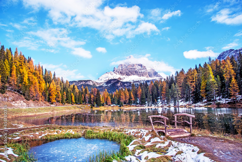 The charming landscape with frozen snowy pond and wooden bridge on a background of Tre Cime de Lavaredo mountains on the Antorno Lake, Dolomites Alps. (Meditation, anti-stress, relaxation - concept)