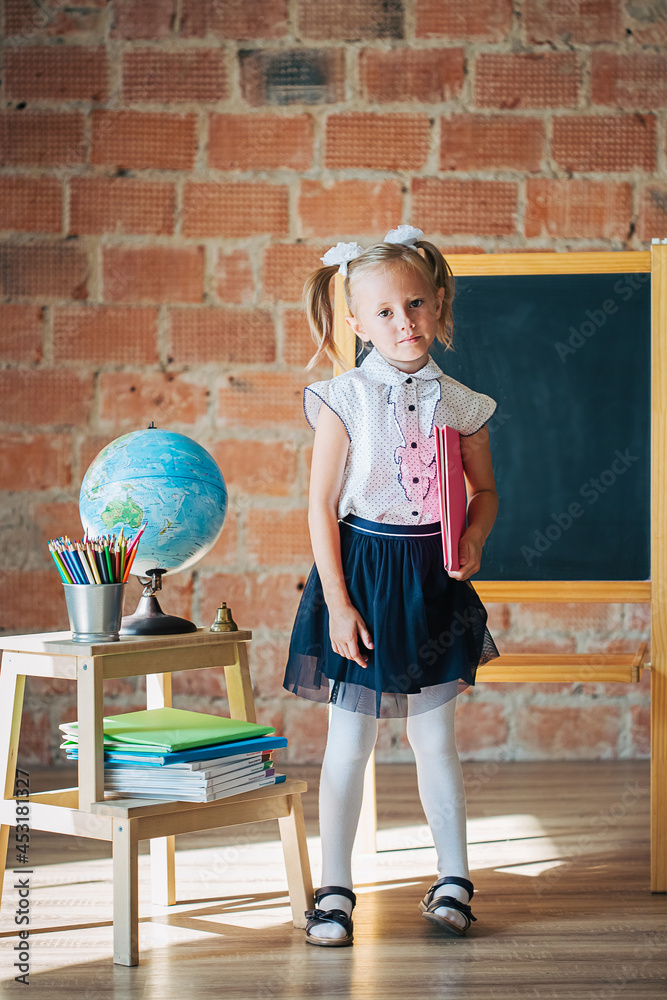 Cute little girl in school uniform posing next to school board with