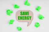 On a white background, there are crumpled green pieces of paper and a wooden sign with the inscription - Save Energy