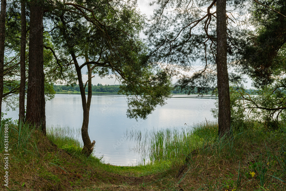 View from the coastline to the blue lake. Rough coast with pine trees in the hills. Summer cloudy day. Nature landscape background View from the coastline to the blue lake. Rough coast with pine trees in the hills. Summer cloudy day. Nature landscape background