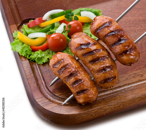 Linguiça toscana no espeto grelhada na braza com salada em fundo de tábua de madeira. photo