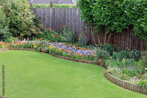 Fototapeta Naklejka Na Ścianę i Meble -  Brightly Coloured Summer Flowers In A Garden Border Surrounded By A Wooden Fence With A Well Maintained Lawn.