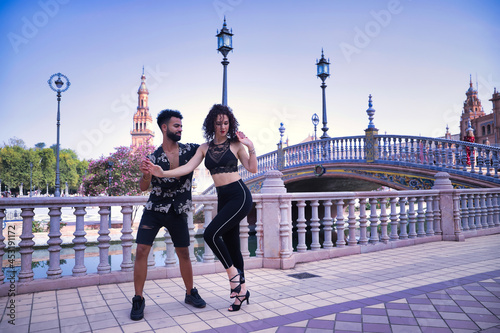 Multi-ethnic young couple doing figures while dancing bachata sensually outdoors.