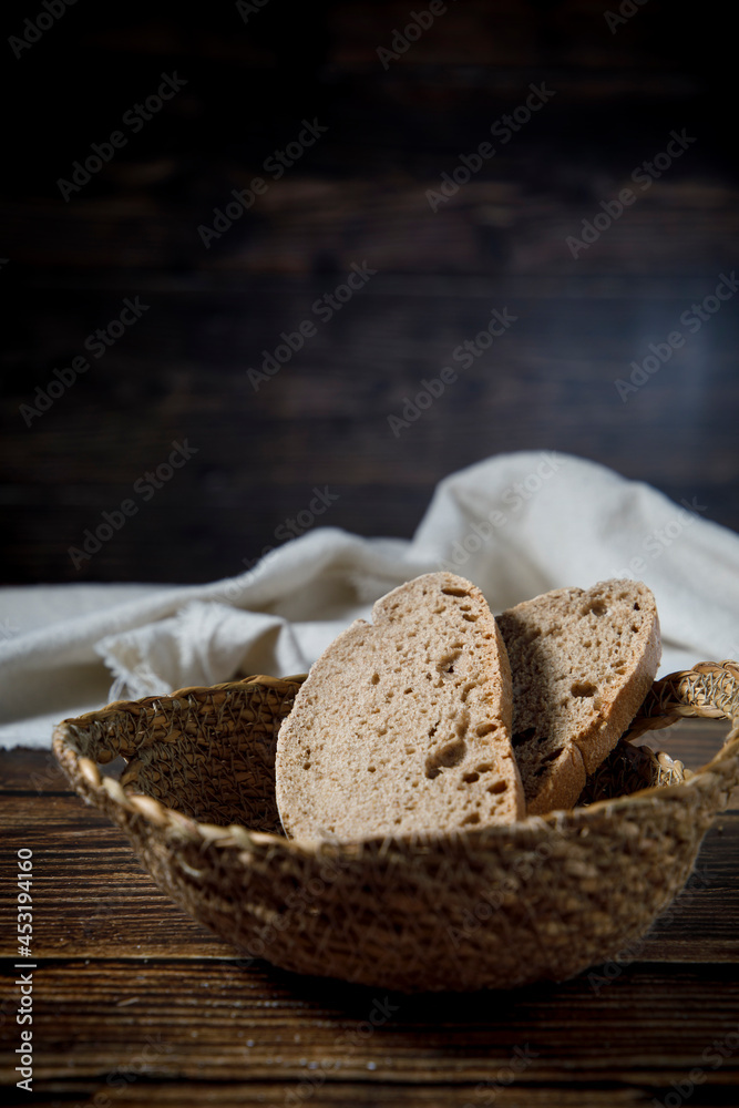 Slices of rustic bread in wicker bowl on a wood table