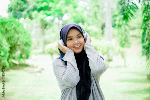 Portrait of an attractive and beautiful young Asian Muslim woman listening to music with headphones in a park