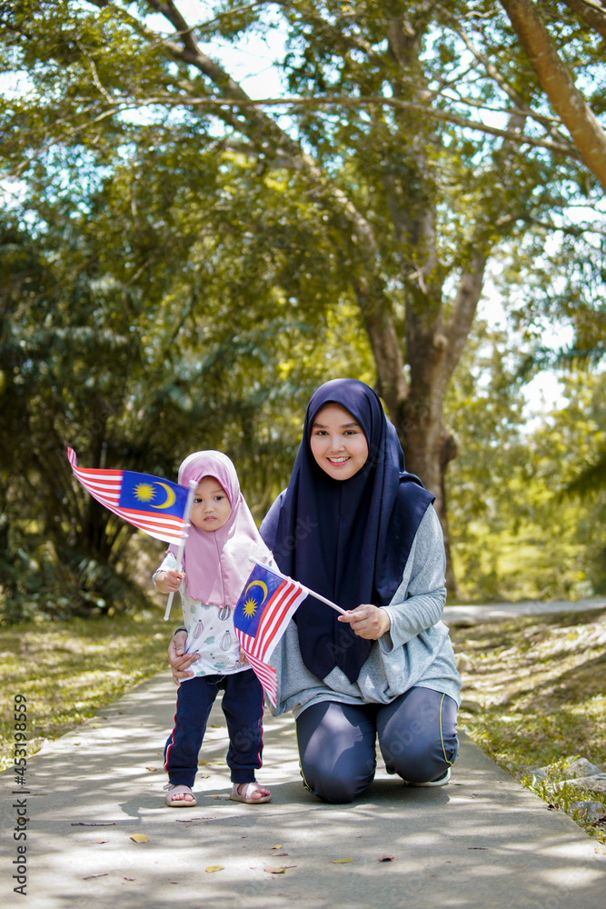 Beautiful young mother with her daughter celebrating Malaysia independence day by raising flag