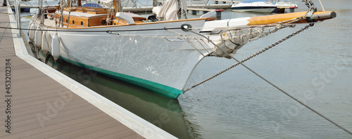 Expensive retro sailing boat (ketch) moored to a pier in a new yacht marina. Wooden teak deck, elegant details. Transportation, nautical vessel, vacations, tourism, cruising, regatta, recreation photo