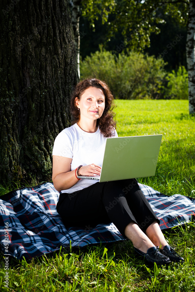 Busy attractive woman working on a laptop sitting on the grass in a city park. Woman studying online outdoors. Freelancer working in the park. Sports girl working remotely. Busy attractive woman working on a laptop sitting on the grass in a city park. Woman studying online outdoors. Freelancer working in the park. Sports girl working remotely.