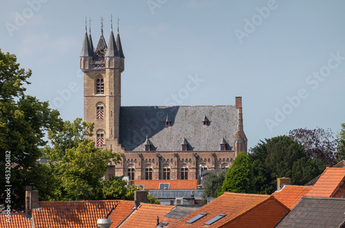 Fototapeta Sluis, the Netherlands - August 5, 2021: The Belfry towering over town houses with red roofs under blue cloudscape