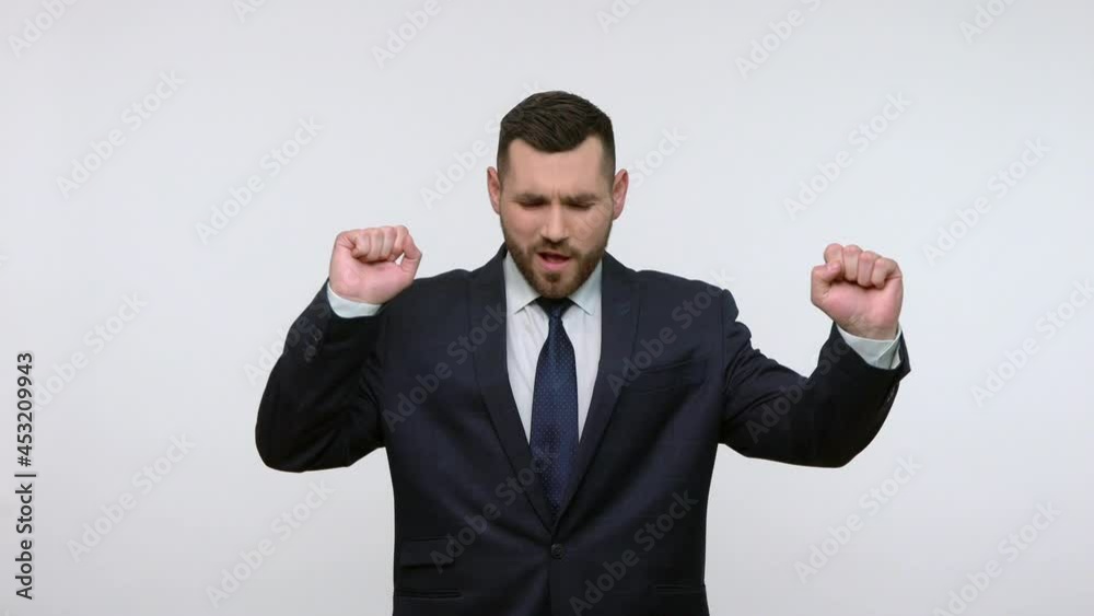 Extremely happy bearded businessman in black official style suit dancing and moving to rhythm, expressing positive emotions, celebrating. Indoor studio shot isolated on gray background. Extremely happy bearded businessman in black official style suit dancing and moving to rhythm, expressing positive emotions, celebrating. Indoor studio shot isolated on gray background.