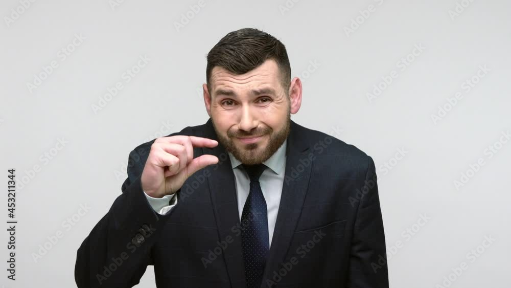 Portrait of disssatisfied bearded businessman in black official style suit showing tiny size, looking sceptic and disappointed with minimum. Indoor studio shot isolated on gray background. Portrait of disssatisfied bearded businessman in black official style suit showing tiny size, looking sceptic and disappointed with minimum. Indoor studio shot isolated on gray background.