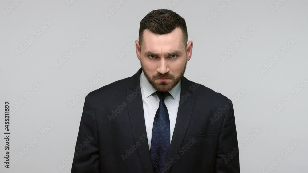 Portrait of angry bearded businessman in black official style suit looking at camera with aggressive expression, swears with an unresponsive employee. Indoor studio shot isolated on gray background. Portrait of angry bearded businessman in black official style suit looking at camera with aggressive expression, swears with an unresponsive employee. Indoor studio shot isolated on gray background.