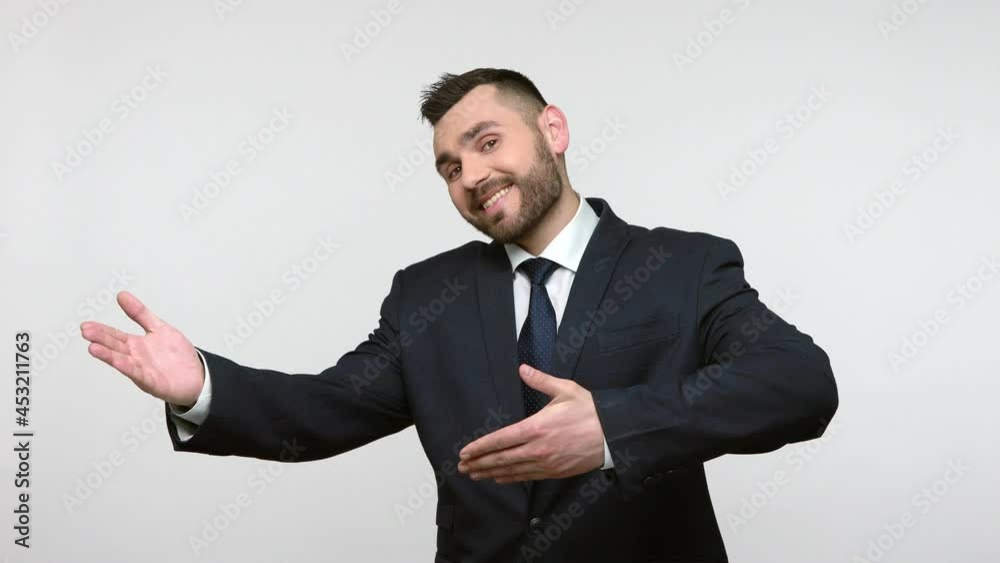 Friendly kind bearded businessman in black official style suit keeping hands wide open to embrace, giving warm hug, welcoming friend. Indoor studio shot isolated on gray background. Friendly kind bearded businessman in black official style suit keeping hands wide open to embrace, giving warm hug, welcoming friend. Indoor studio shot isolated on gray background.