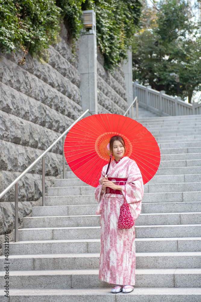 Beautiful Asian woman tourism in pink traditional japanese kimono dress  holding red umbrella walking in city street with happiness. Smiling kimono  girl enjoy summer outdoor lifestyle activity in Japan Stock Photo
