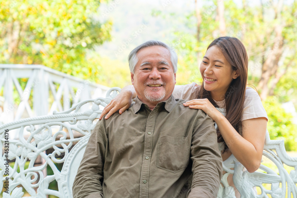 Asian woman caring and hugging senior man grandfather sitting on outdoor chair in the park. Elderly retired male relax and enjoy outdoor activity together with daughter. Family relationship concept Asian woman caring and hugging senior man grandfather sitting on outdoor chair in the park. Elderly retired male relax and enjoy outdoor activity together with daughter. Family relationship concept
