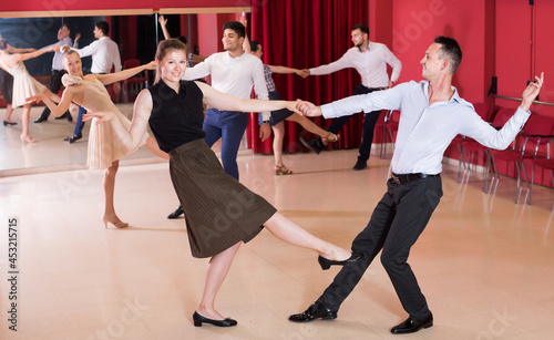 Glad people dancing lindy hop in pairs in dance hall