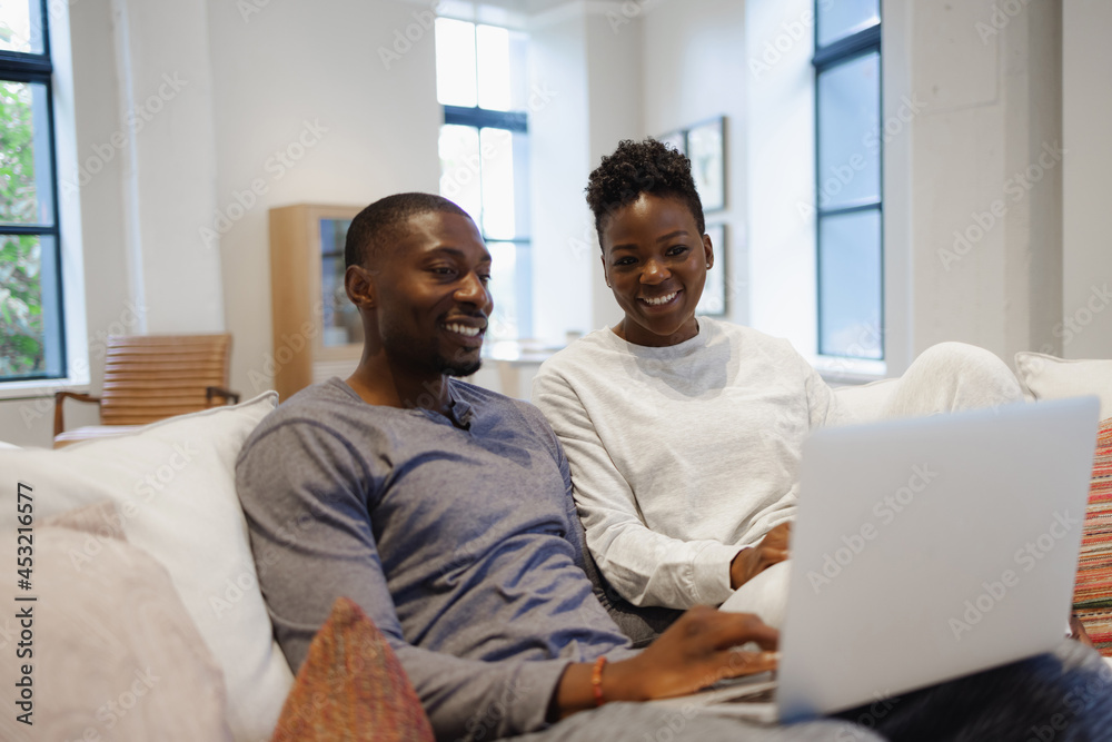 African American Smiling couple sitting on sofa and using laptop African American Smiling couple sitting on sofa and using laptop
