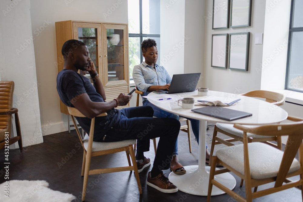 Black Man and woman using laptop and smart phone at table Black Man and woman using laptop and smart phone at table