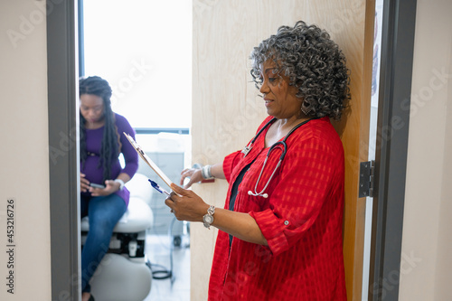 Female doctor with medical record knocking on clinic exam room door, Black Senior doctor and young woman patient 