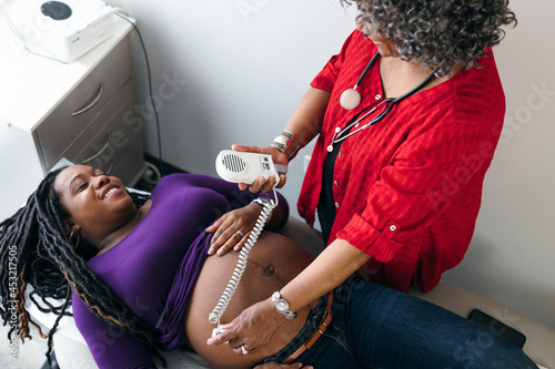 Female doctor uses sonogram doppler to listen to fetal heartbeat, Black pregnant patient  photo