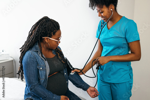 Black woman nurse checks vitals of pregnant patient photo