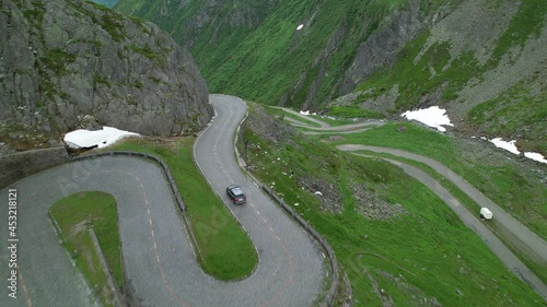 DRONE: Grey colored tourist car cruises along the scenic switchback road of Passo San Gottardo. Tourists on road trip across the mountains of Switzerland drive along hairpin turns of Gotthardpass. photo