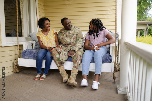 Military dad talks with wife and daughter on front porch swing, African American photo