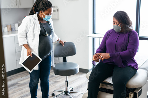 Pregnant doctor entering exam room to see senior woman patient photo