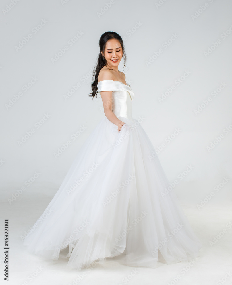 Full length of young attractive Asian woman, soon to be bride, wearing white wedding gown looking happy spinning. Concept for pre wedding photography