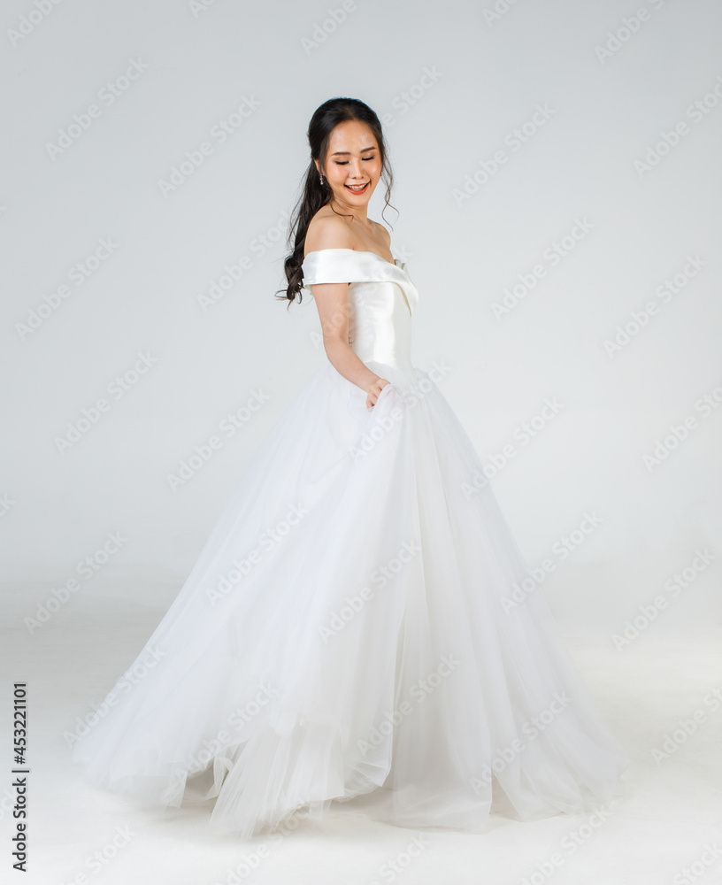 Full length of young attractive Asian woman, soon to be bride, wearing white wedding gown looking happy spinning. Concept for pre wedding photography Full length of young attractive Asian woman, soon to be bride, wearing white wedding gown looking happy spinning. Concept for pre wedding photography