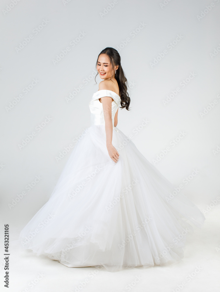 Full length of young attractive Asian woman, soon to be bride, wearing white wedding gown looking happy spinning. Concept for pre wedding photography Full length of young attractive Asian woman, soon to be bride, wearing white wedding gown looking happy spinning. Concept for pre wedding photography