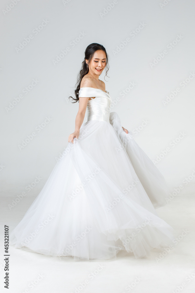 Full length of young attractive Asian woman, soon to be bride, wearing white wedding gown looking happy spinning. Concept for pre wedding photography Full length of young attractive Asian woman, soon to be bride, wearing white wedding gown looking happy spinning. Concept for pre wedding photography