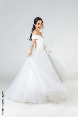 Full length of young attractive Asian woman, soon to be bride, wearing white wedding gown looking happy spinning. Concept for pre wedding photography