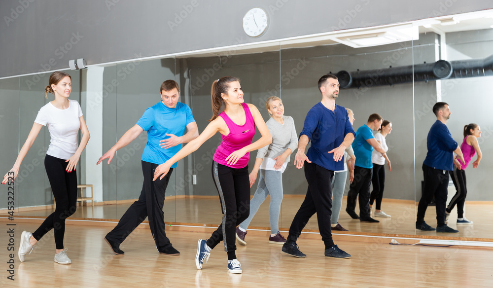 Smiling females and males doing Zumba dance workout during group classes in fitness center