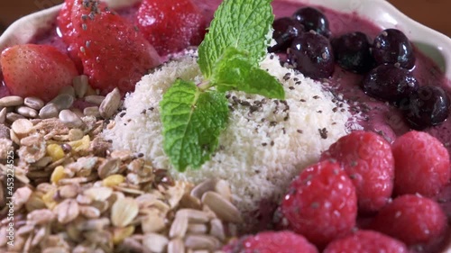 smoothie bowl with Strawberries, Oats, Grains and Blueberries in a White Bowl Close Up Spinning on Table. photo