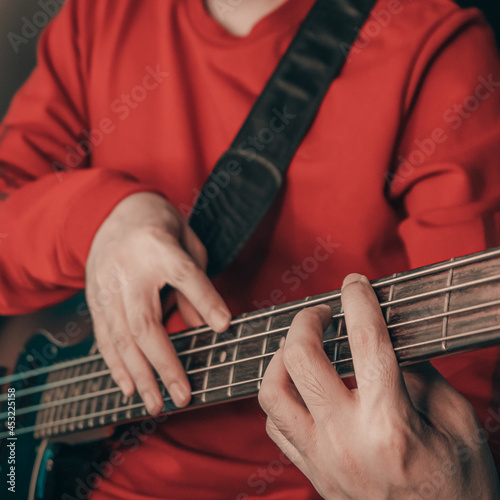 Man is playing electric bass guitar blurred black background.