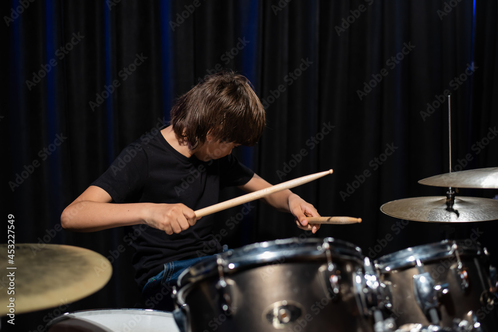 Fototapeta premium The boy learns to play the drums in the studio on a black background. Music school student