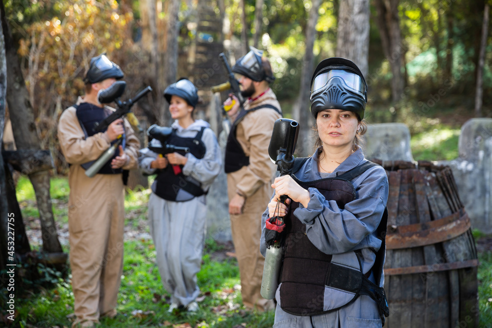 Fototapeta premium Portrait of young woman paintball player with marker gun ready for game outdoors